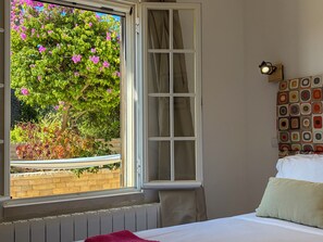 A bedroom with a large window, a bed with white bedding, a wall-mounted light fixture, and a patterned headboard. - LV Premier Algarve AB1 (Tavira)