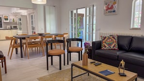 Ein modernes Wohnzimmer mit einem schwarzen Ledersofa, einem Holzesstisch und Stühlen. Auf dem Couchtisch steht eine Blumenvase und ein Buch.