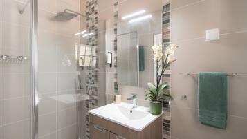 Un baño moderno con cabina de ducha de vidrio, un lavamanos blanco y una planta verde, además de una toalla color turquesa.