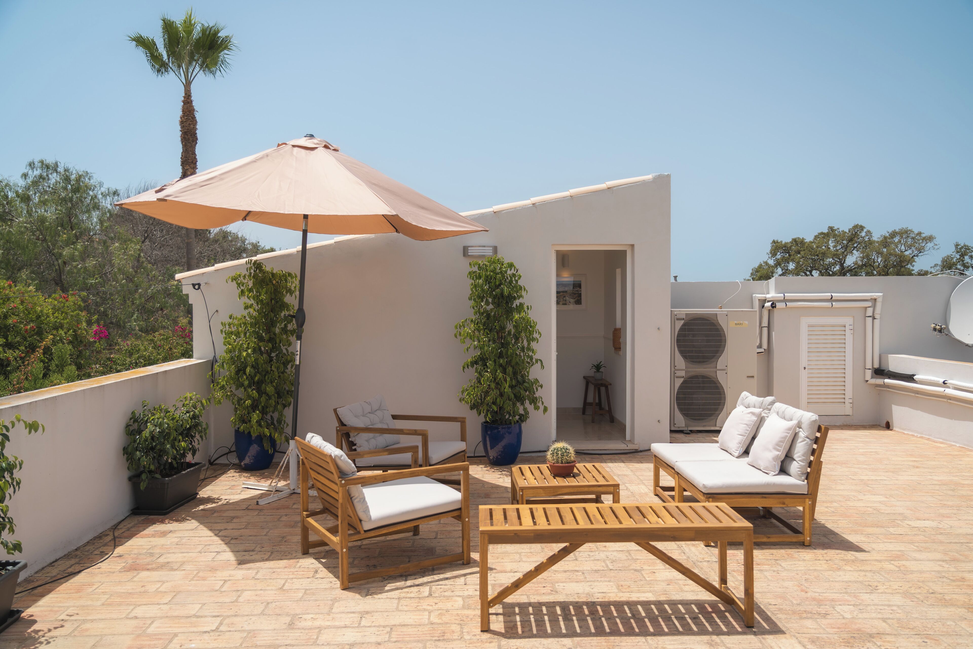 Eine Terrasse im Freien mit einem Holztisch und Stühlen, einem großen Sonnenschirm und Blumentöpfen.