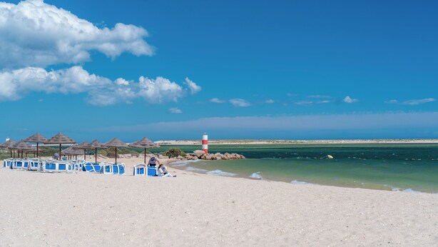 Ein Strand mit Sonnenschirmen, Liegestühlen und einem Leuchtturm.