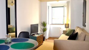 Una habitación con cama, televisión, mesa de comedor y ventana con cortinas.
