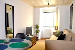 Ein Zimmer mit einem Bett, einem Fernseher, einem Esstisch und einem Fenster mit Vorhängen.