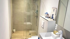 A modern bathroom with a glass-enclosed shower, a white toilet, a sink with a mirror, and a blue cabinet. - Modern, comfortable apartment located 200 meters from the beach and 1 km from shops (Roquebrune-sur-Argens)