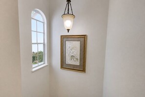 Un pasillo con un amplio ventanal de arco, una obra de arte enmarcada y una lámpara colgante.