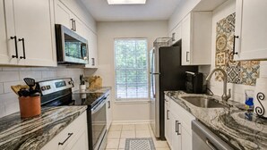 A compact kitchen with white cabinets, a microwave, a refrigerator, and a window with blinds. - 189 Cordero Cottage Ln (Hot Springs)