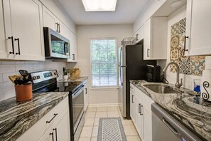 Una cocina compacta con armarios blancos, un microondas, un refrigerador y una ventana con persianas.