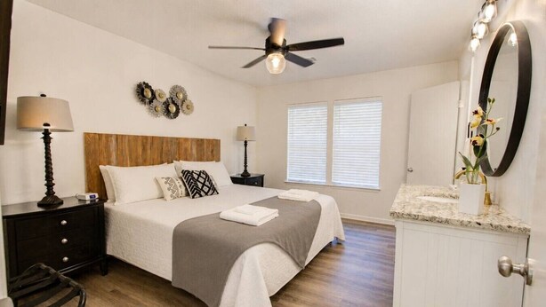A bedroom with a bed, bedside lamps, a ceiling fan, a nightstand, a dresser, and a window with blinds. - 189 Cordero Cottage Ln (Hot Springs)