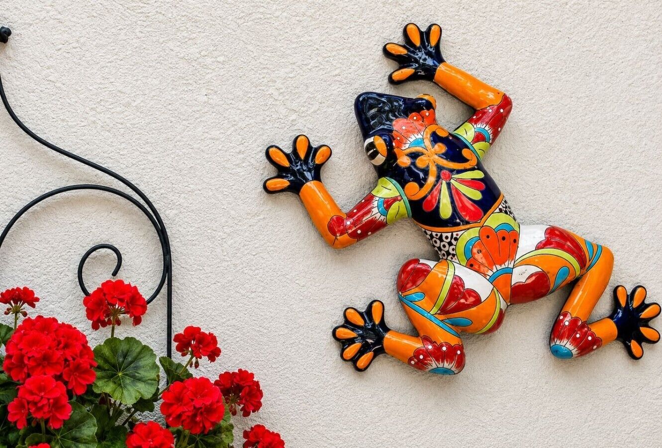 A colorful ceramic frog decoration on a textured wall, a black cable, and red flowers.