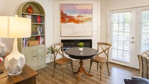 A dining area with a round table, two chairs, a bookshelf, a fireplace, and a door with blinds. - 189 Cordero Cottage Ln (Hot Springs)