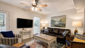 A living room with a television, a ceiling fan, a coffee table, a sofa, and a painting on the wall. - 189 Cordero Cottage Ln (Hot Springs)