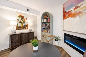 A dining area with a round table, two chairs, a bookshelf, a painting, and a fireplace. - 189 Cordero Cottage Ln (Hot Springs)