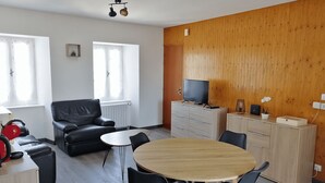 A modern living room with a sofa, a dining table with chairs, a TV on a cabinet, and a wooden accent wall. - Cozy 2-bedroom apartment with a large balcony - Montsalvy (Montsalvy)