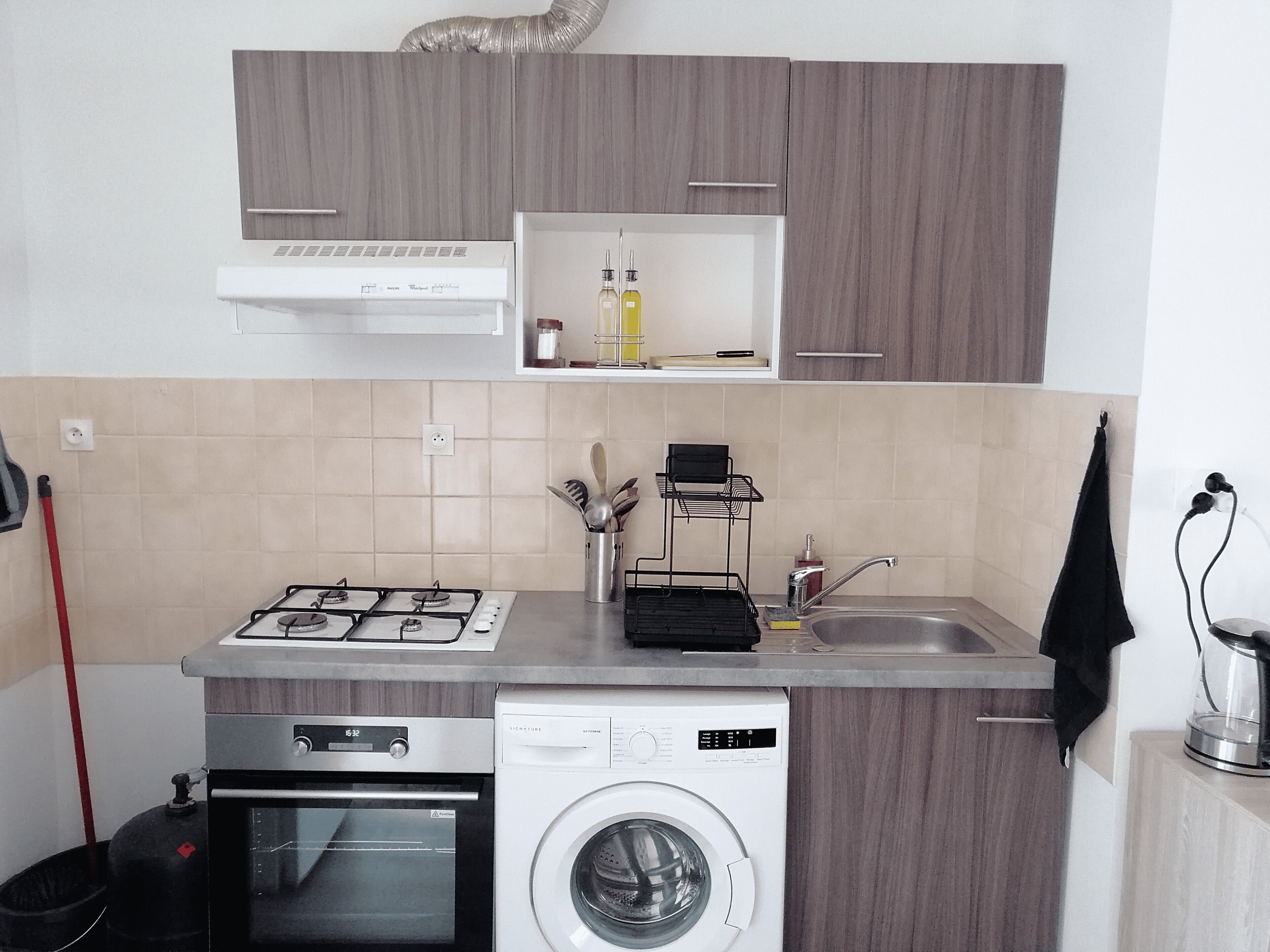 Een kleine keuken met een gasfornuis, oven en een voorlader wasmachine.