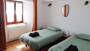 A bedroom with two beds, a window with curtains, a radiator, and a wall-mounted mirror. - Cozy 2-bedroom apartment with a large balcony - Montsalvy (Montsalvy)
