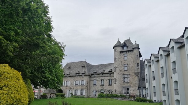 A historic stone building with a central tower, surrounded by a well-maintained lawn and a large tree. - Cozy 2-bedroom apartment with a large balcony - Montsalvy (Montsalvy)