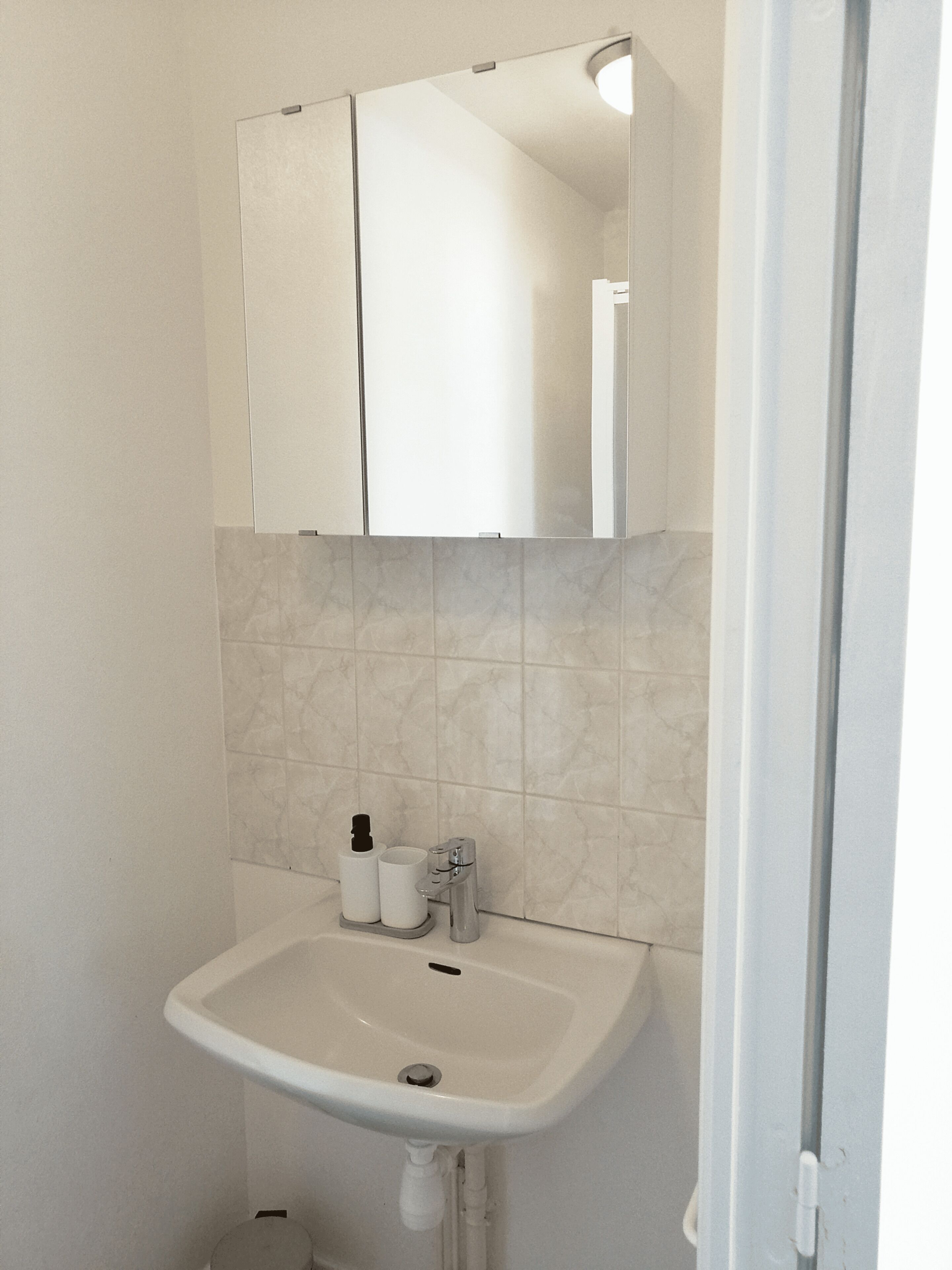 Een badkamer met een witte wastafel, een spiegel erboven en een betegelde wand.