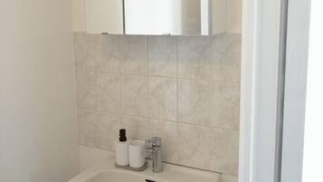 Een badkamer met een witte wastafel, een spiegel erboven en een betegelde wand.
