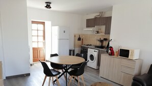 A compact kitchen with a washing machine, a microwave, and a dining area with a round table and chairs. - Cozy 2-bedroom apartment with a large balcony - Montsalvy (Montsalvy)