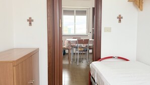 A bedroom with a bed, a wooden wardrobe, and a dining area with chairs and a table. - SE278 – Senigallia, seafront two-bedroom apartment with balconies and parking space (Senigallia)