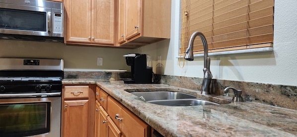 A kitchen with wooden cabinets, a stainless steel sink, a microwave, and a coffee maker.