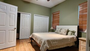 Une chambre à coucher avec un lit, une table de chevet, une lampe, une commode et un placard dont la porte est ouverte.