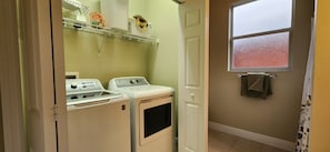 A laundry room with two washers and dryers, a shelf with laundry supplies, and a window with a view of the outside.