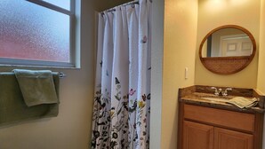 Une salle de bain avec un rideau de douche, un lavabo avec un miroir et un porte-serviettes.