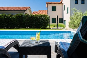 Ein Poolbereich mit Liegestühlen, einem Tisch mit einem Getränk und einem Gebäude mit einem Ziegeldach im Hintergrund.