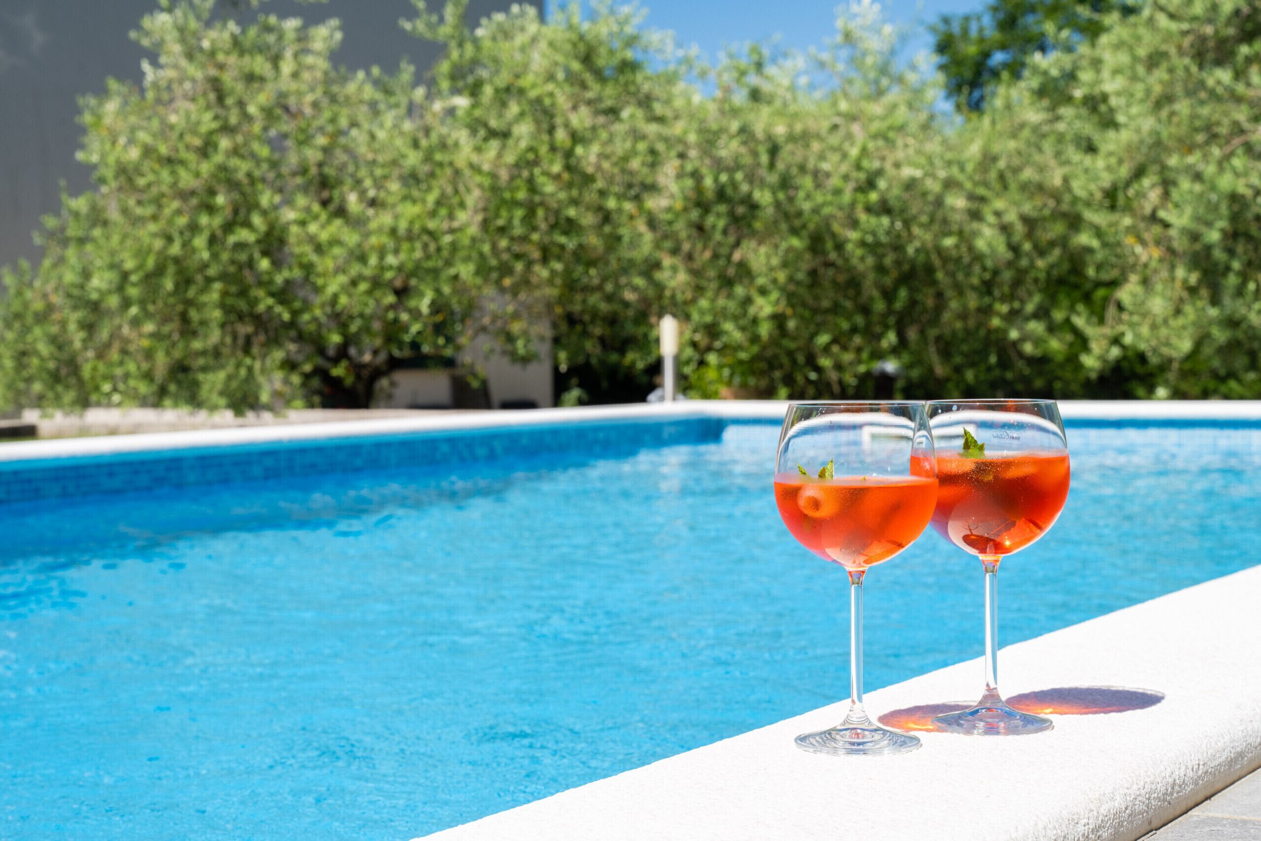 Ein Swimmingpool mit zwei Gläsern roter Flüssigkeit am Rand.