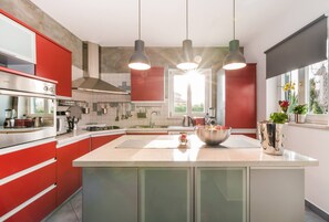 Een moderne keuken met rode kastjes, roestvrijstalen apparatuur en hanglampen.