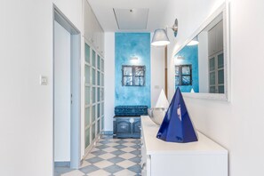 Ein Flur mit einem Schachbrettmuster-Boden, einer blauen Akzentwand, einem Spiegel und einem blauen Dekorationsgegenstand auf einer weißen Ablagefläche.