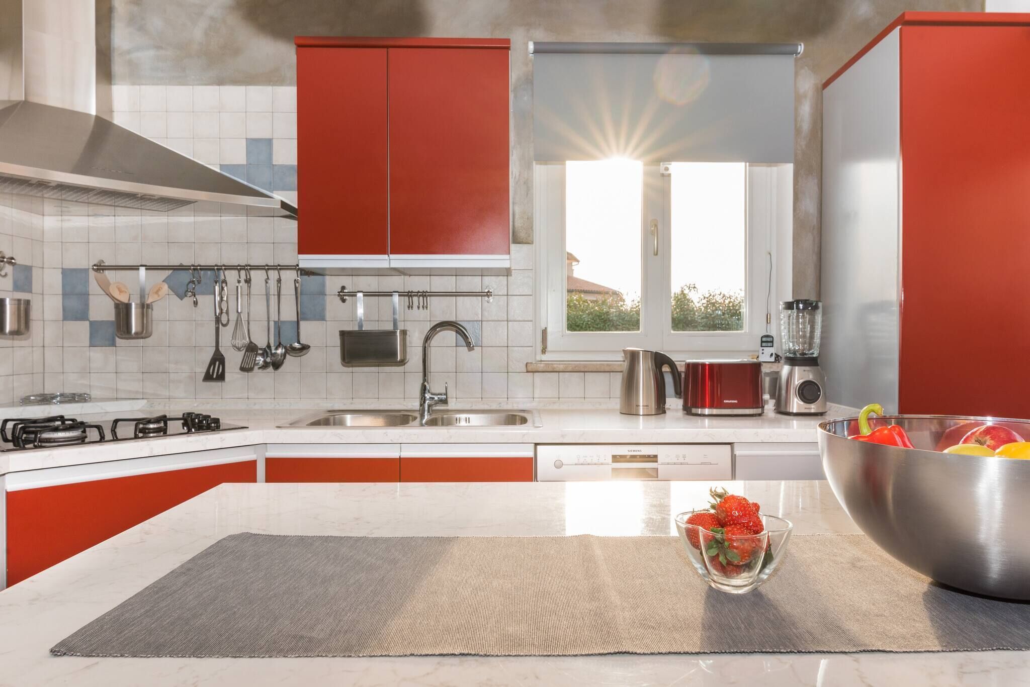 A modern kitchen with red cabinets, stainless steel appliances, and a large window.