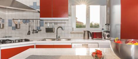 A modern kitchen with red cabinets, stainless steel appliances, and a large window.