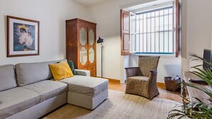 Un salon comprenant un canapé, un fauteuil en osier, une armoire, un tableau encadré et une fenêtre avec des barreaux.
