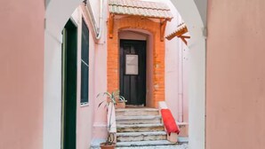 Une ruelle étroite avec un bâtiment rose, une porte et un objet rouge posé sur les marches.