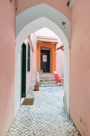 A narrow alleyway with a pink building, a door, and a red object on the steps. - Renovated Historic Apartment with an Enclosed Terrace (Lisboa)