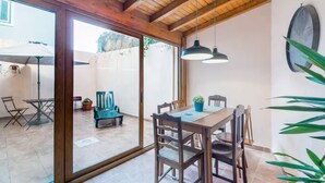 Un coin repas avec une table et des chaises en bois, une plante en pot et une vue sur une terrasse extérieure, visible à travers une porte vitrée.