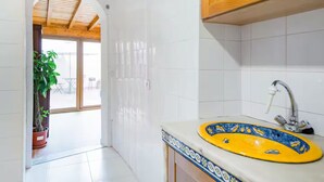 Une cuisine moderne avec des carreaux blancs, un évier jaune à motifs bleus, des meubles en bois et une plante en pot.