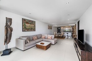 Ein modernes Wohnzimmer mit einem Ecksofa, einem Couchtisch und einem Fernseher. Im Hintergrund befindet sich ein Essbereich mit Stühlen und einem Tisch.