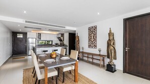A modern dining area with a table set for four, a kitchen in the background, and decorative statues. - Best Sea Views Walk Surin Beach- Sunsuri C297 (Choeng Thale)