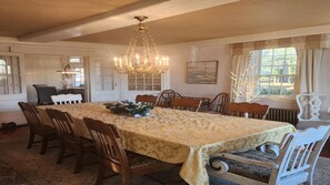 A dining room with a large table, chairs, a chandelier, and a window with curtains. - Oceanview Classic Maine Cottage within 1 minute. (York)