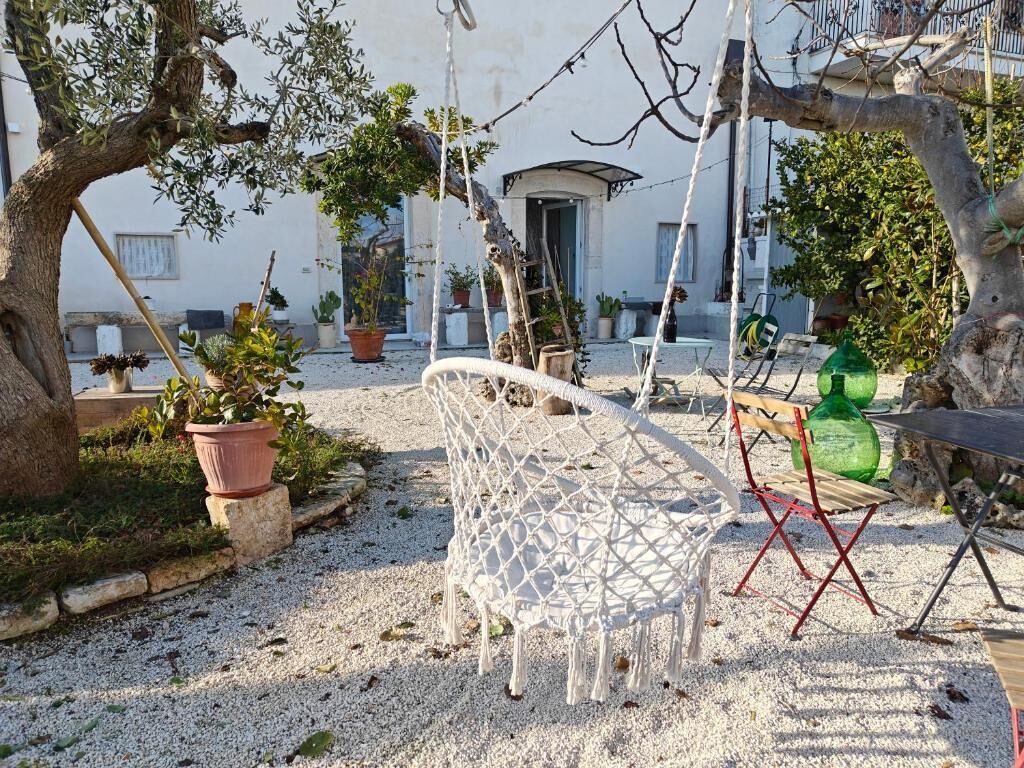 A garden with a white macrame chair, potted plants, and a building in the background.