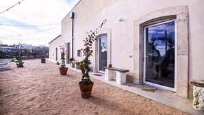 A building with a gravel courtyard, potted plants, and a large glass door. - Masseria Casino Ciomme  (Gioia del Colle)