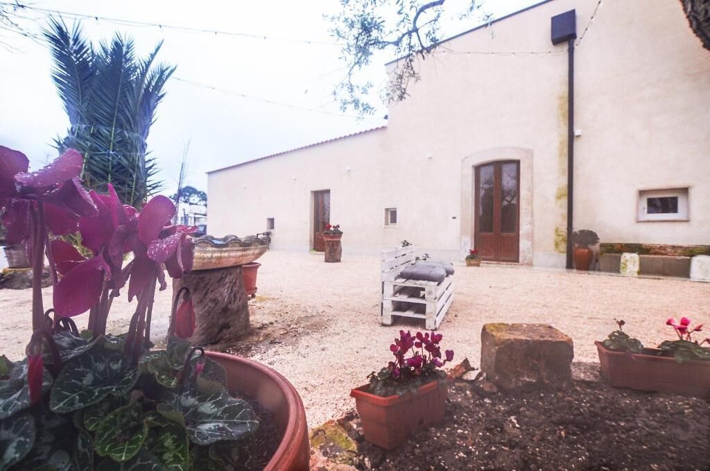 Une cour avec des plantes en pot, un banc en bois et un bâtiment doté d’une porte et de fenêtres.