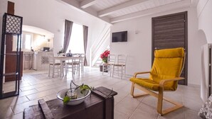 A living room with a yellow armchair, a dining area with white furniture, and a kitchen in the background. - Masseria Casino Ciomme  (Gioia del Colle)