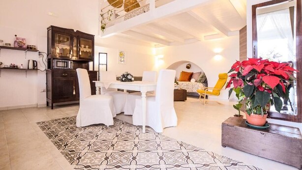 A spacious living area with a dining table, chairs, a sofa, a yellow armchair, a potted plant, and a kitchen area with a microwave and cabinets. - Masseria Casino Ciomme  (Gioia del Colle)