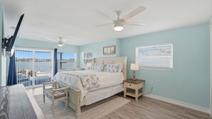 Un dormitorio con cama, mesitas de noche, ventilador de techo y vistas al exterior por una puerta corredera.