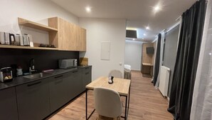 A modern kitchen with dark cabinets, a wooden countertop, and a dining area with a table and chair. - Apartmenthaus Zeuthen 3 (Zeuthen)