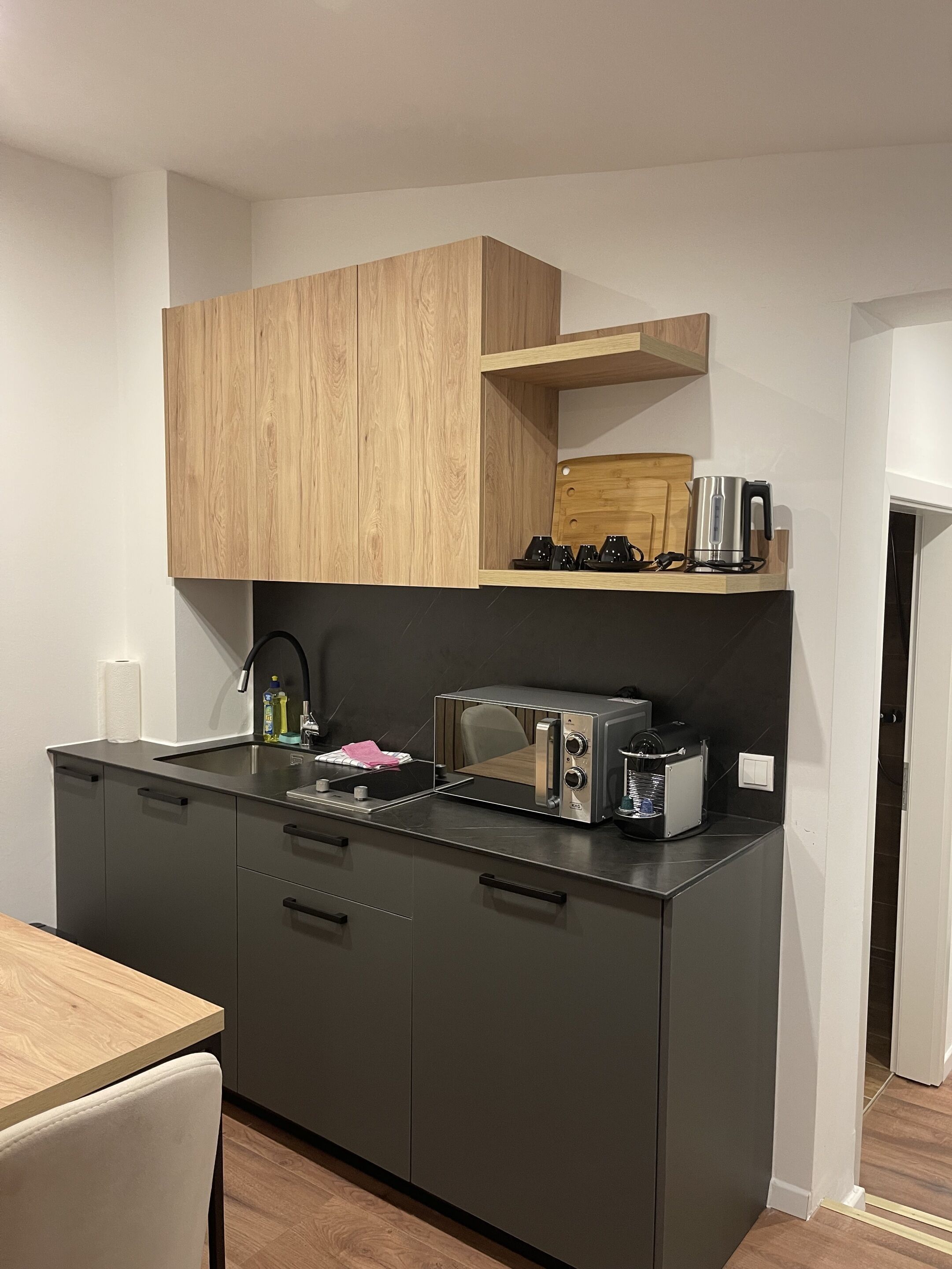A modern kitchen with dark cabinetry, a wooden upper shelf, and a built-in toaster.